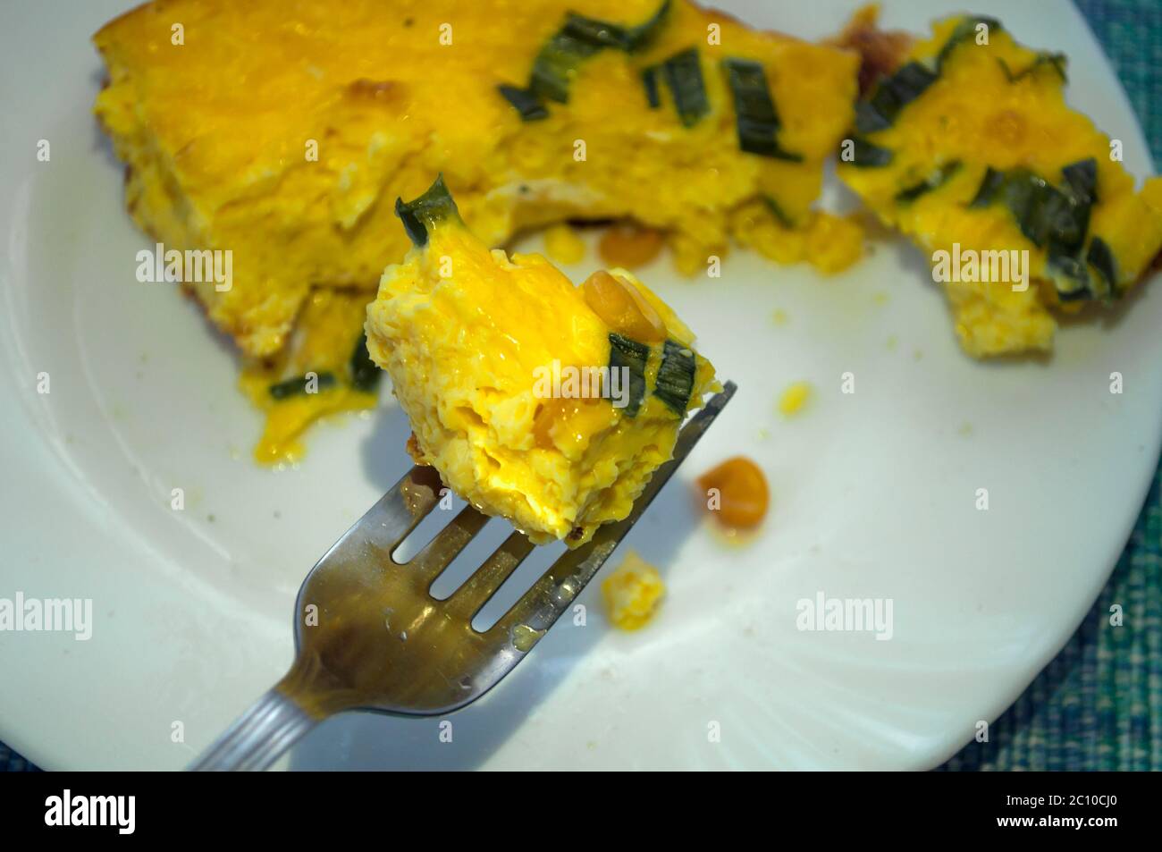 Auf einem weißen Teller gelbes Omelett mit Grüns und Mais. Gabel auf der linken Seite, Linkshänder. Omelette auf einer Gabel Stockfoto