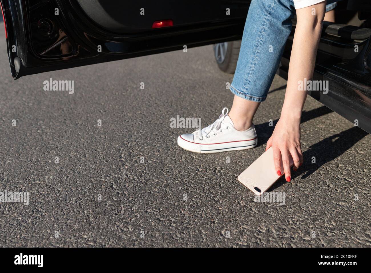 Frau stieg in ein Auto und ließ Smartphone auf Asphalt fallen, brach das Glas auf der Rückseite und nahm ein kaputtes Telefon vom Boden. Stockfoto