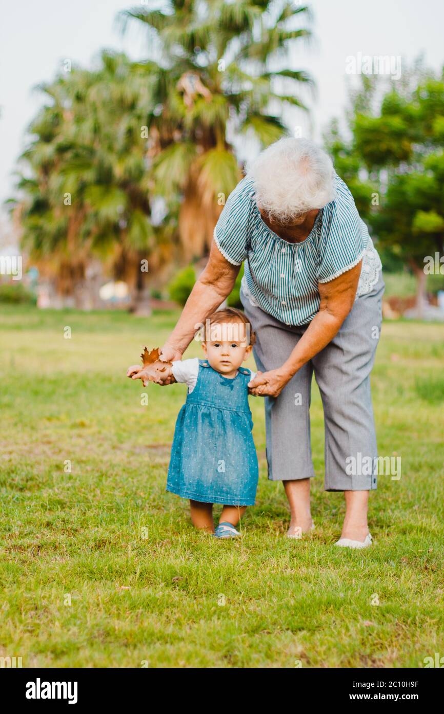 Eine Großmutter mit europäischem Auftritt und einer einjährigen Enkelin spazieren in einem grünen Park. Stockfoto