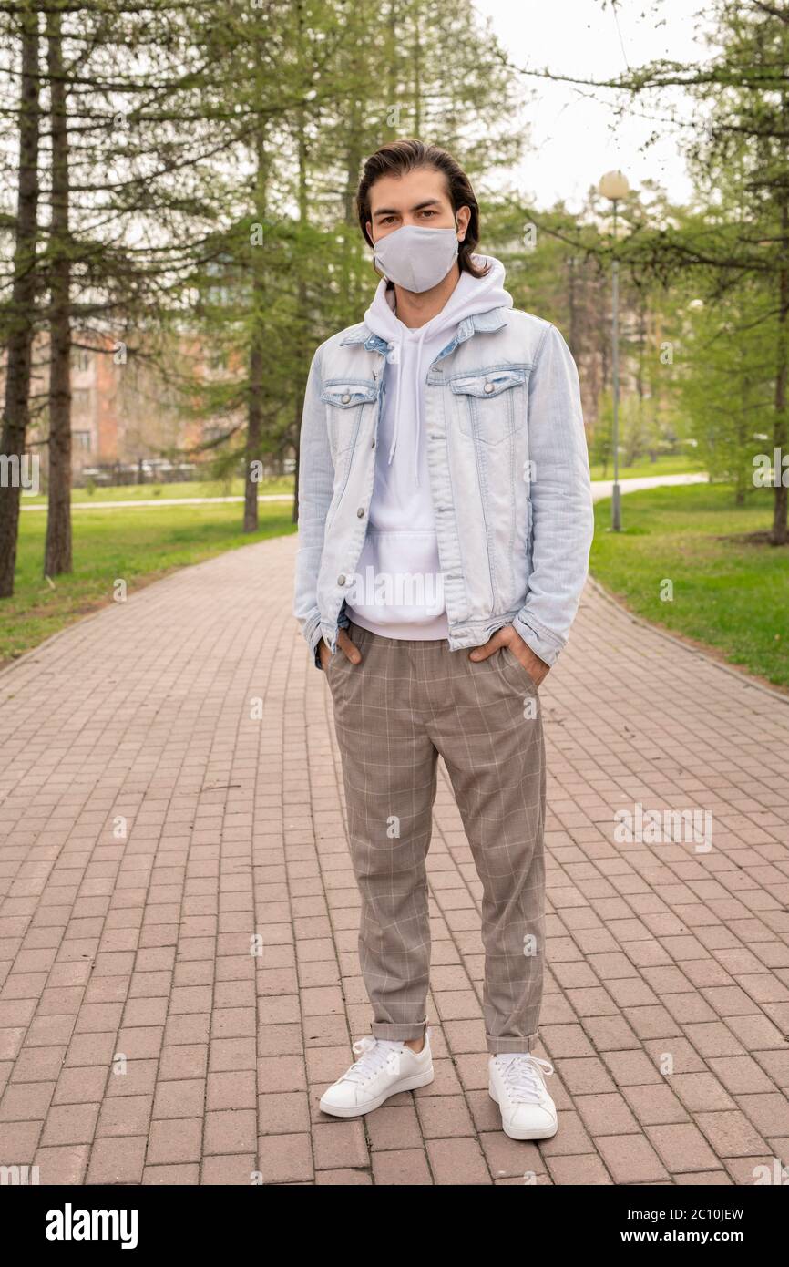 Schöner Mann in lässigem Outfit und Stoffmaske, der während der Coronavirus-Pandemie im Stadtpark spazieren geht Stockfoto