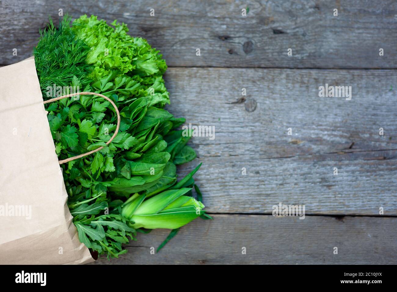 Frisches Gemüse in einem Papierbeutel - grüne Zwiebeln, Dill, Petersilie, Spinat, Rucola, Sauerampfer. Lieferung von Lebensmitteln und frischem Gemüse nach Hause. Holzhintergrund Stockfoto