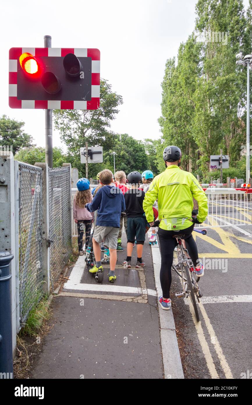 Ein Radfahrer und eine Gruppe kleiner Kinder warten am Bahnübergang Vine Road von Network Rail in Barnes, im Südwesten Londons, England, Großbritannien Stockfoto
