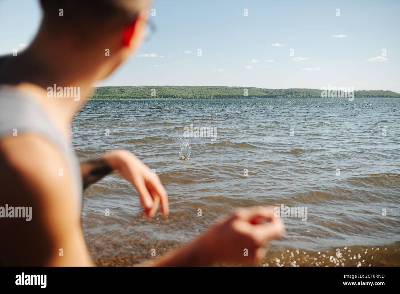 Mann, der an einem schönen Tag am See flache Steine gegen ein Wasser hüpft Stockfoto