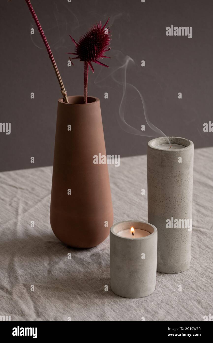 Hygge Stil Komposition aus brennenden und ausgeblasen Kerzen in weißen Keramikgläsern und braun handgemachte Tonvase mit zwei getrockneten Blumen Stockfoto