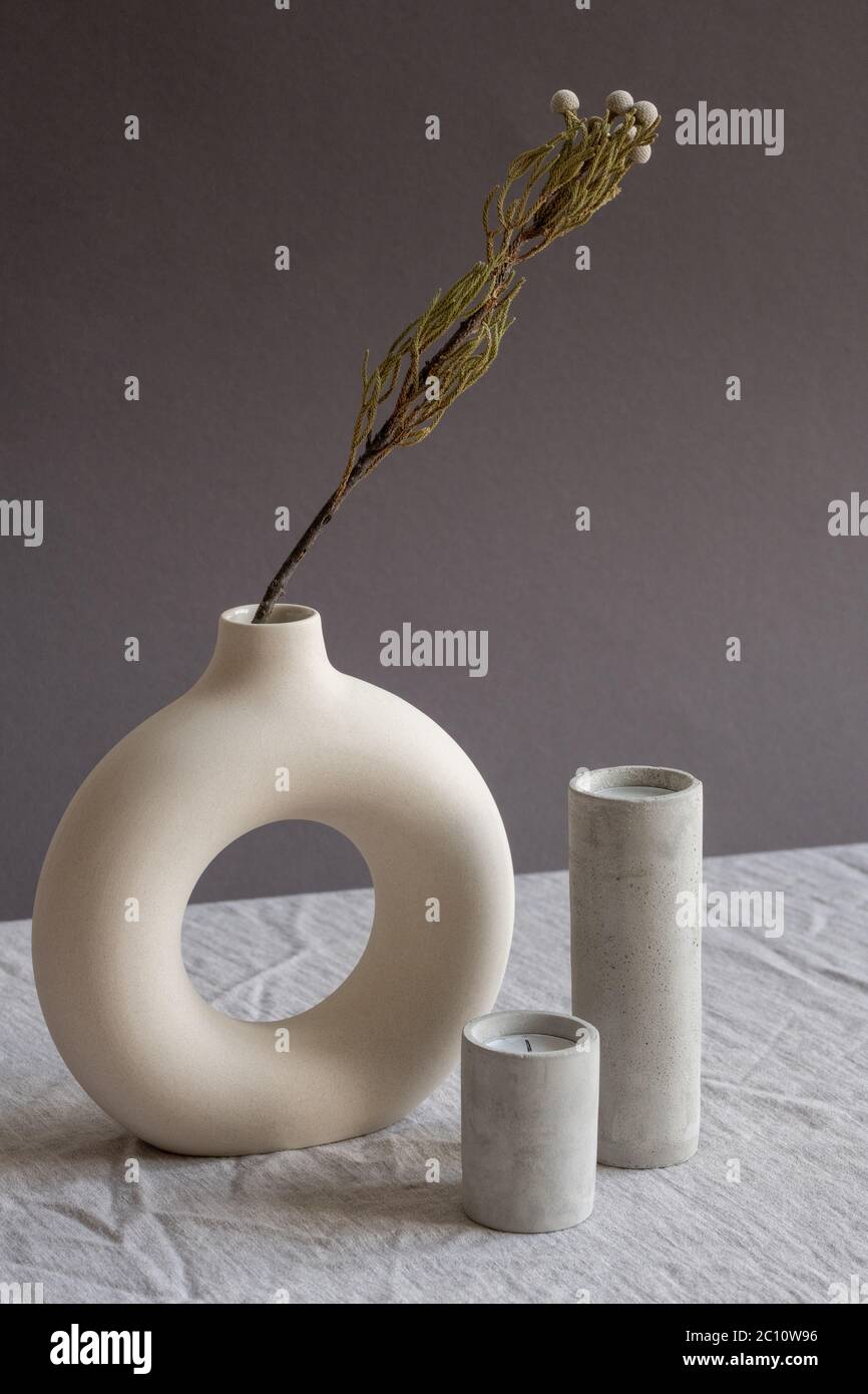 Komposition aus zwei aromatischen, ausgeblasenen Kerzen in weißen Keramikgläsern, die von einer kreativen handgefertigten Vase mit getrockneten Blumen auf dem Tisch stehen Stockfoto