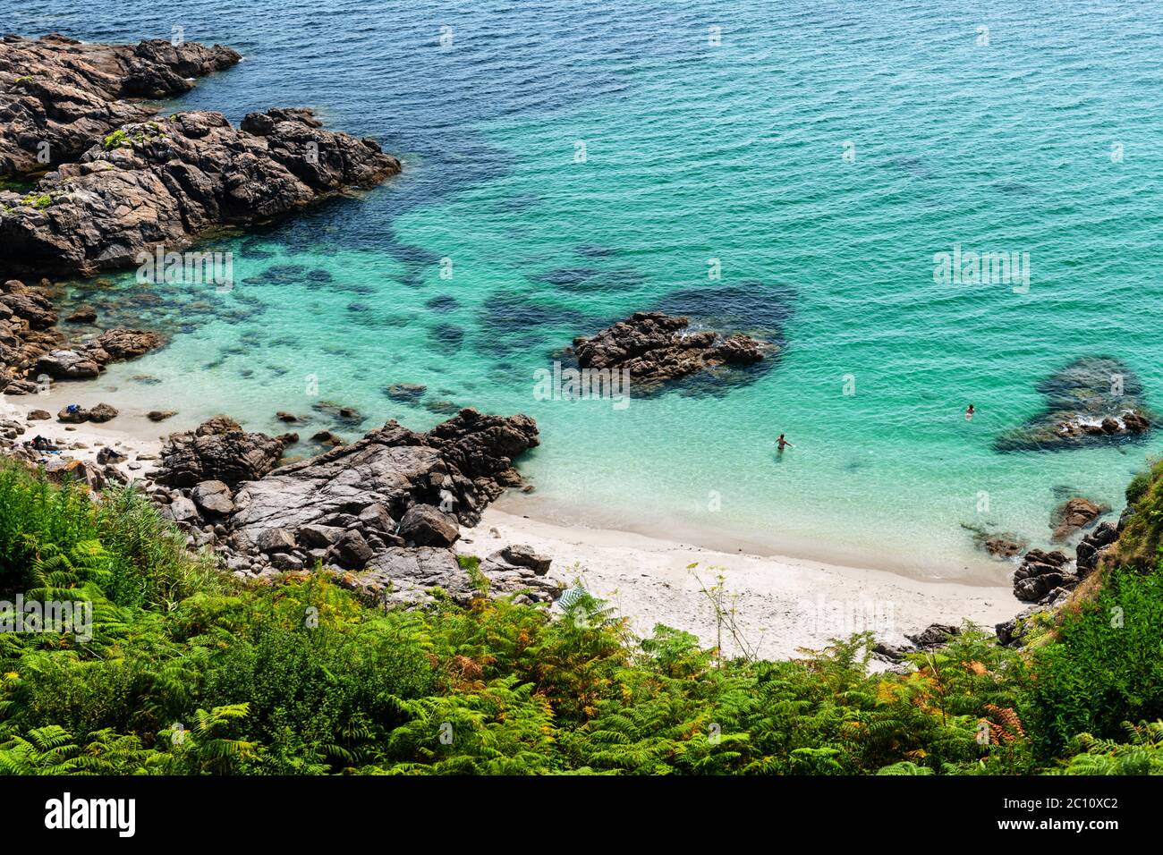 Versteckte Bucht in Finisterre an einem späten Sommernachmittag in Galicien, Spanien, mit zufälligen Badegäste im Wasser. Stockfoto