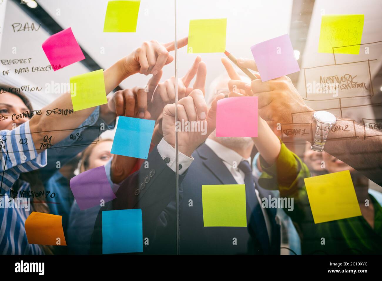 Das Team von Leuten bei der Arbeit im Büro zeigt mit der Hand einen Post-it auf dem Glas Stockfoto