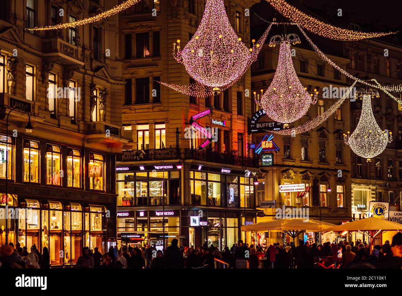 Nachtansicht der Grabenstraße mit Weihnachtsbeleuchtung, beleuchteten Fenstern der Geschäfte, hängenden großen Kronleuchtern und vielen Touristen zu Fuß, Wien. Stockfoto