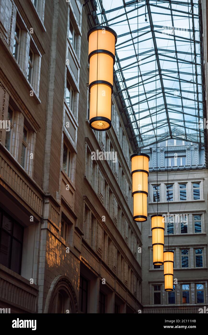 Blick auf glühende mit gelbem Licht große, zylindrische, Pendelleuchten in einem Durchgang mit einem Glasdach. Stimmungsvolle Beleuchtung mit warmweißem Licht. Stockfoto