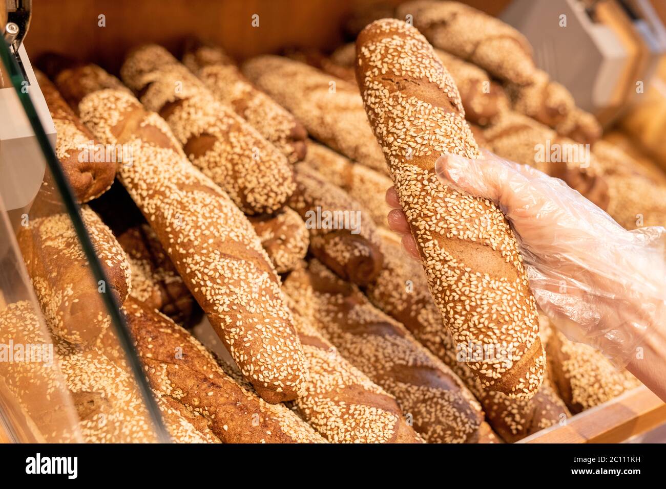 Hand der weiblichen Kundin in Handschuh, die frisches Baguette aus Brot Display beim Besuch Supermarkt und Lebensmittelprodukte kaufen Stockfoto