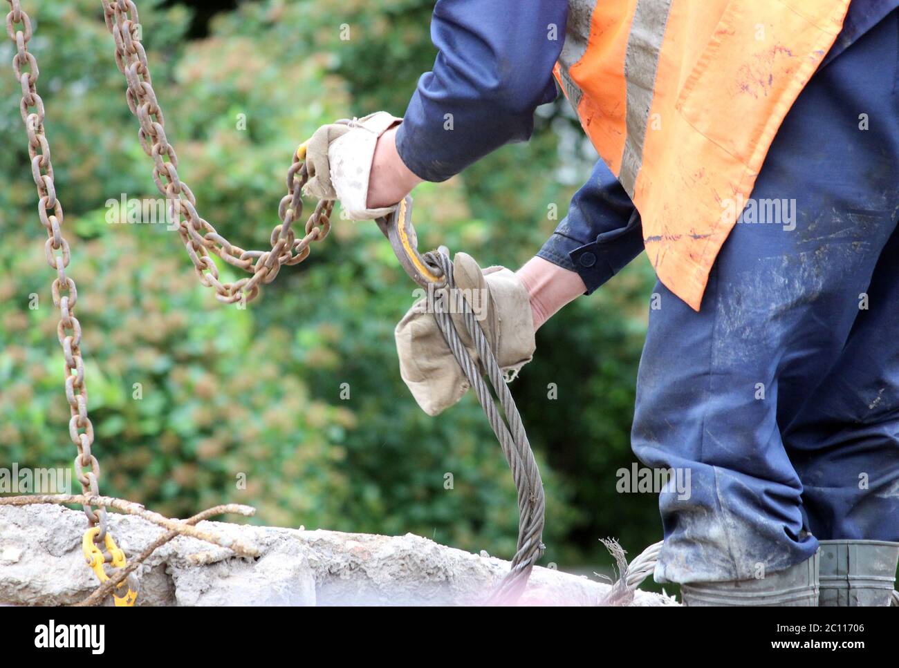 Arbeiter berührt die Kranhaken an den Schlaufen in der Betonplatte bei Reparaturarbeiten. Stockfoto