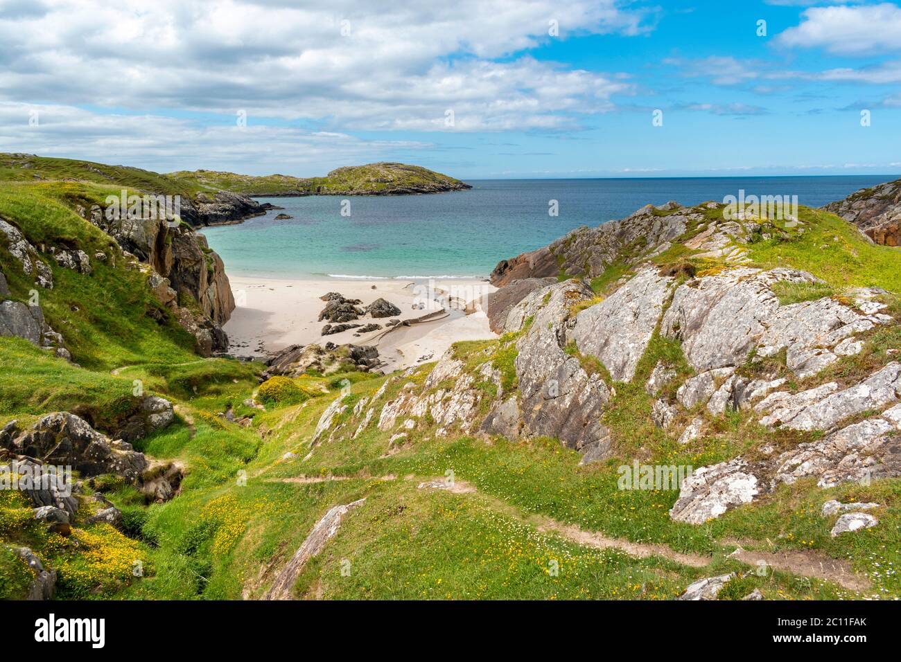 ACHMELVICH BAY UND STRAND SUTHERLAND HIGHLANDS SCHOTTLAND EIN BLAUER HIMMEL EIN TÜRKISFARBENES MEER UND EIN PFAD ZWISCHEN GELBEN BLUMEN VON VÖGELN FUSS TREFOIL LO Stockfoto