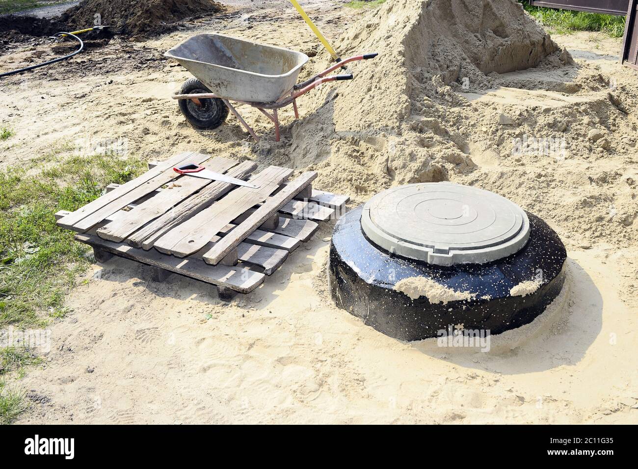 Baustelle mit neuen bewaffneten Schächten, Wagen, Sand und Ausrüstung Baustelle mit neuen bewaffneten Schächten, Wagen, Sand und Eq Stockfoto