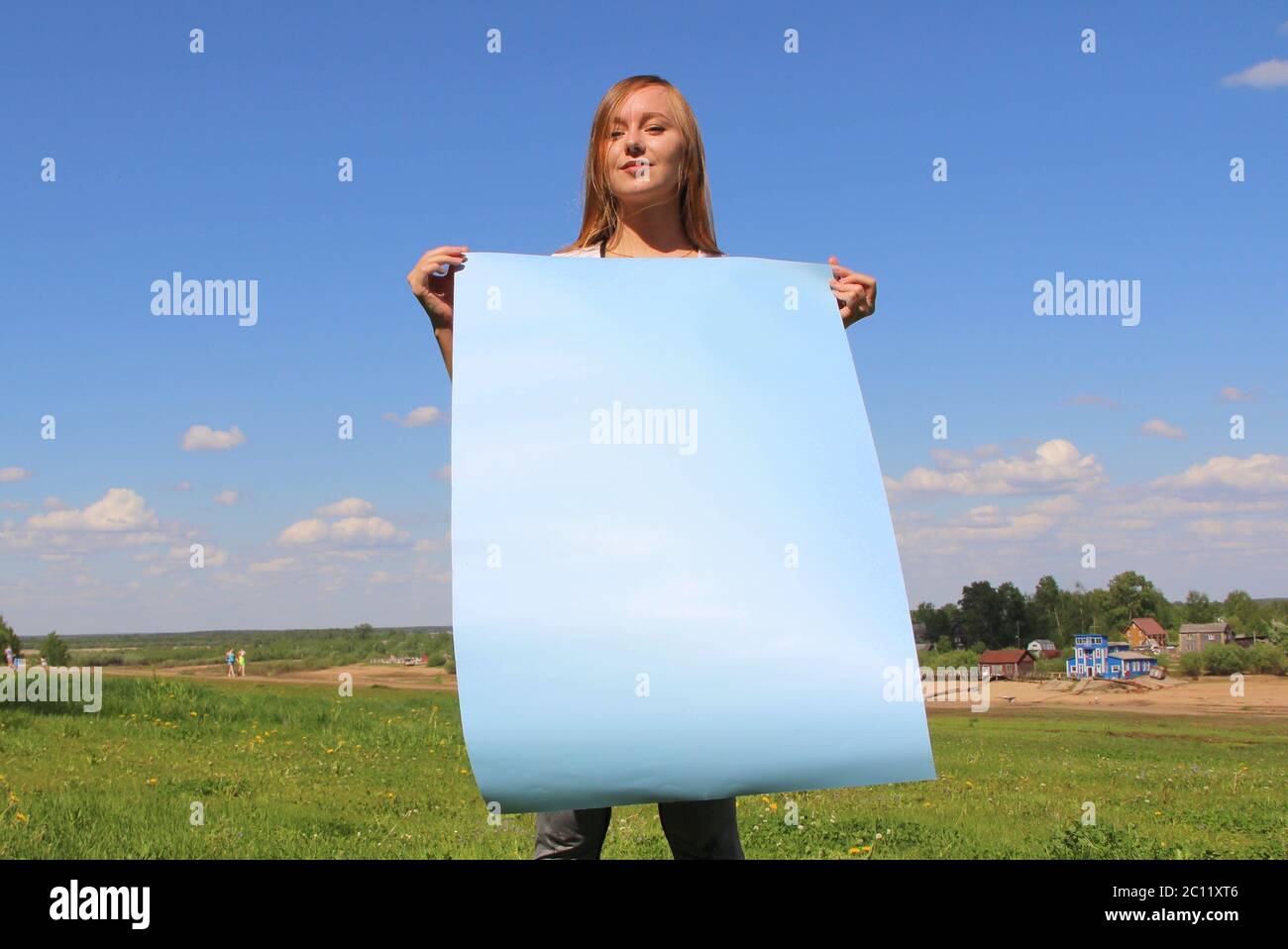 Ein schönes langhaariges Mädchen auf dem grünen Gras auf dem Rasen hält ein leeres blaues Poster. Layout für Design, Platz für Text, Kopierraum. Stockfoto
