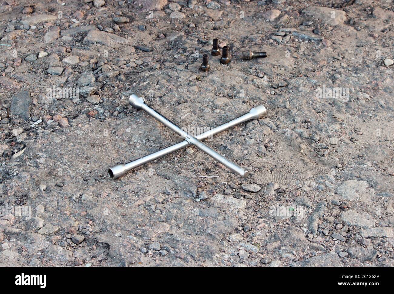 Schlüssel Cross Road und vier Muttern liegen auf dem Boden während der Reparatur Auto. Stockfoto