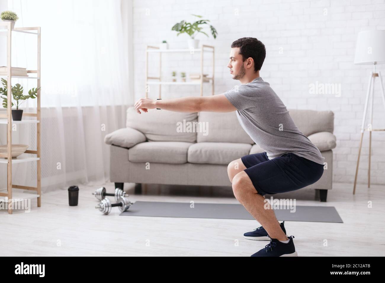 Bleiben Sie allein zu Hause für das Training. Mann hockt im Wohnzimmer Innenraum zu Hause Stockfoto