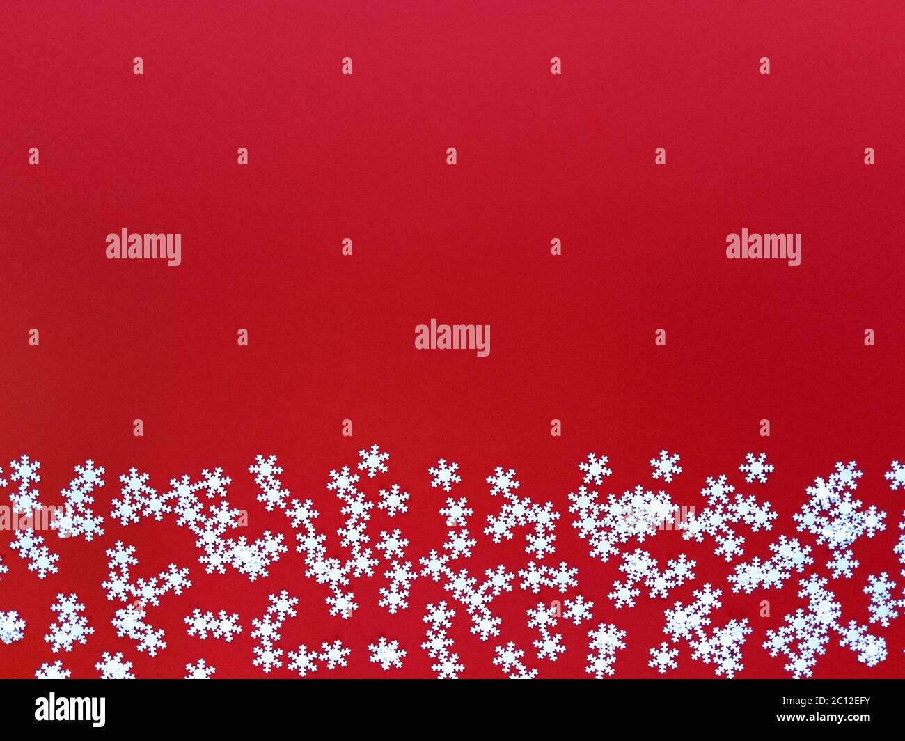 Verstreute weiße Schneeflocken auf rotem Hintergrund. Einfaches, flaches Lay mit Kopierplatz. Stock Foto. Stockfoto