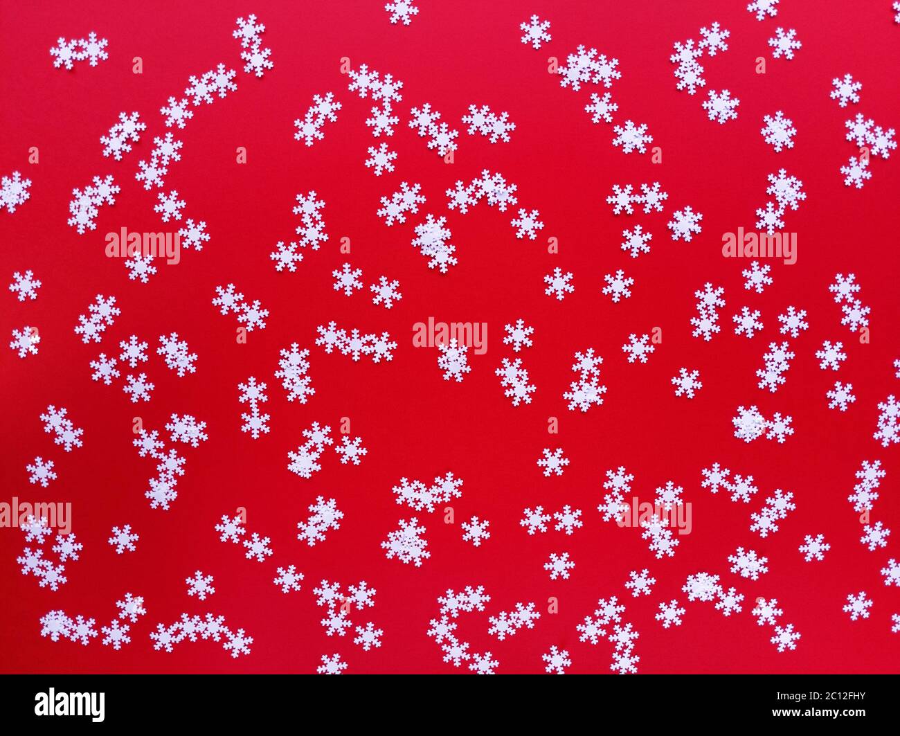 Verstreute weiße Schneeflocken auf rotem Hintergrund. Einfache festliche flache Laie. Stock Foto. Stockfoto