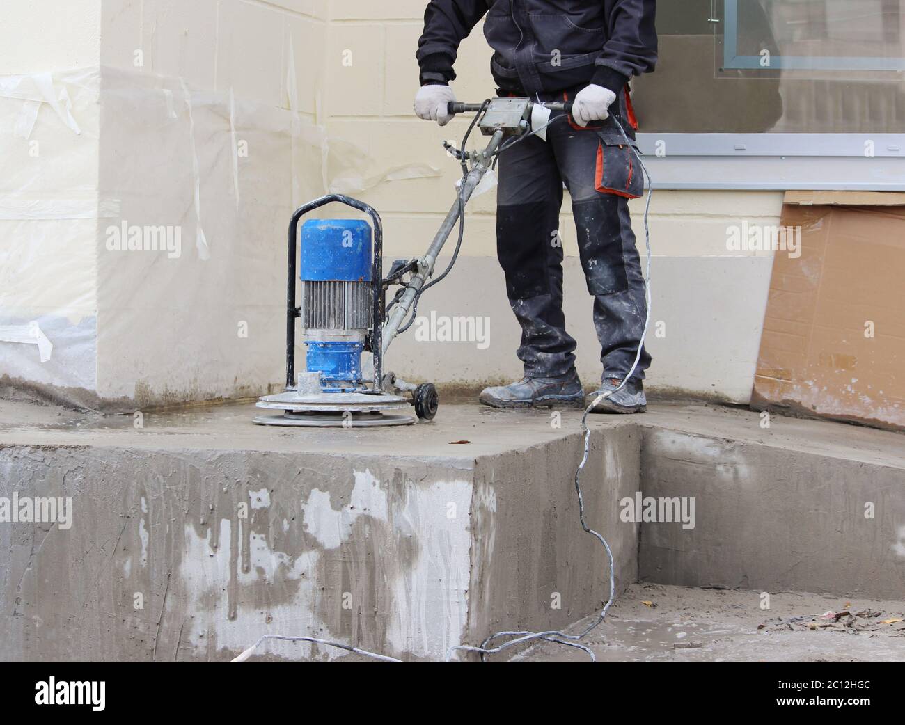 Männliche Arbeiter arbeitet mit der Diamant-Schleifmaschine, Polieren der Veranda vor dem Bürogebäude. Der Zementboden und Stockfoto