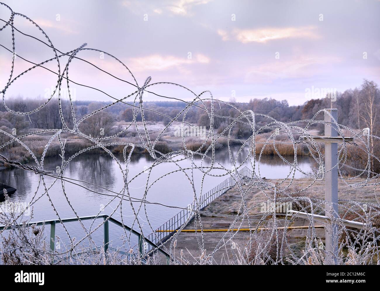 Stellen Sie einen Zaun Stacheldraht im Winter im Frost in der Dämmerung Stockfoto
