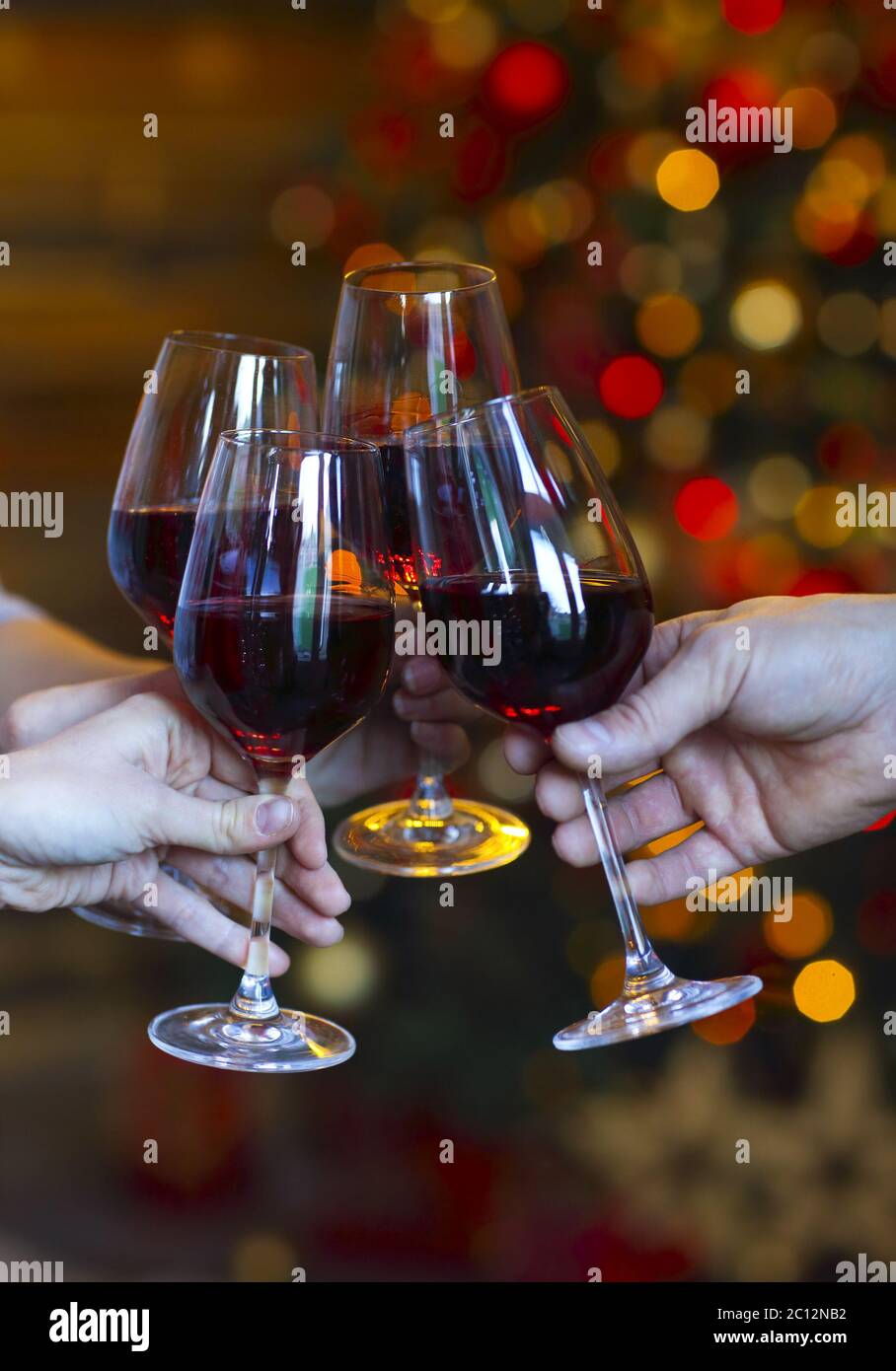 Klirrende Gläser Wein in den Händen auf hellen weihnachtslichtern Hintergrund Stockfoto