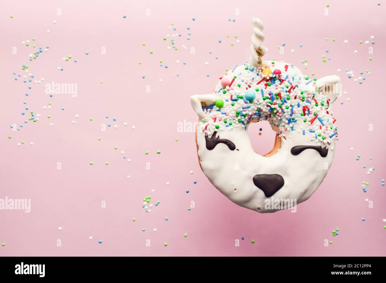 Einhorn Donut schwebt in der Luft über rosa Hintergrund. Trendy donut Einhorn mit weissen Fliegen Glasur. Ansicht von oben. Kopieren Sie Platz. Stockfoto