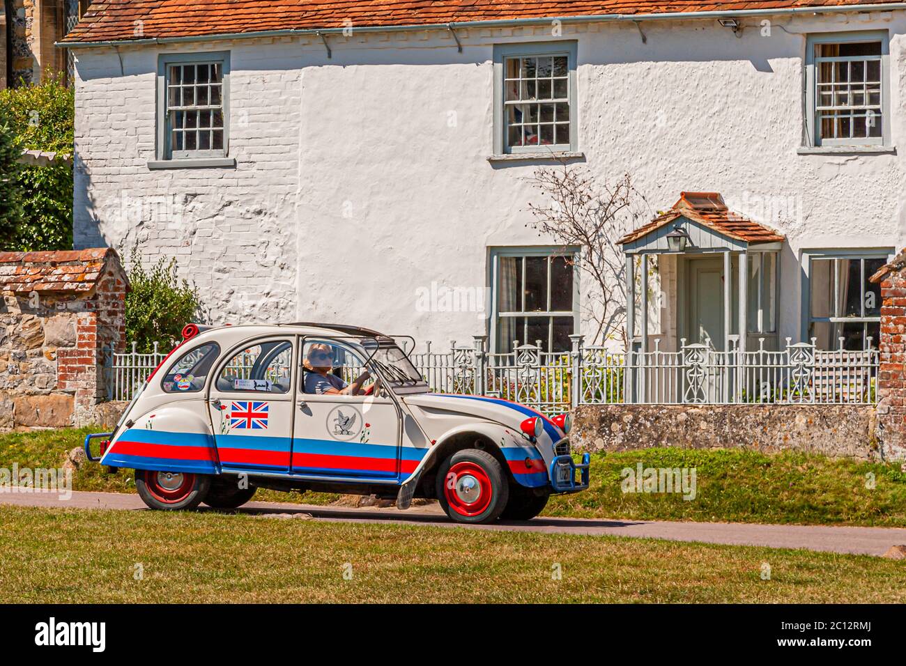 Ein Citroën 2CV, der mit dem Union Jack und den Farben der britischen Flagge bemalt ist, fährt an einem weiß getünchten Cottage in Aldbourne, Wiltshire, England vorbei. Stockfoto