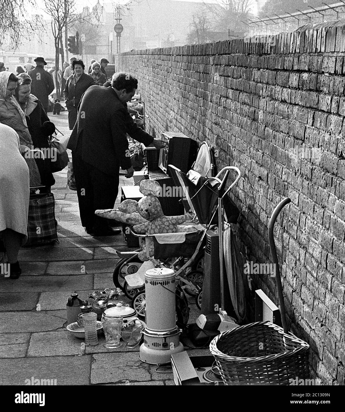 AJAXNETPHOTO. FEBRUAR 1975. PORTSMOUTH, ENGLAND. - FLOHMARKT - IN DER UNICORN ROAD; KÄUFER STÖBERN DURCH GEBRAUCHTE WAREN UND KLEIDUNG AUF DEM BÜRGERSTEIG.FOTO:JONATHAN EASTLAND/AJAX REF:7513 5 122 Stockfoto