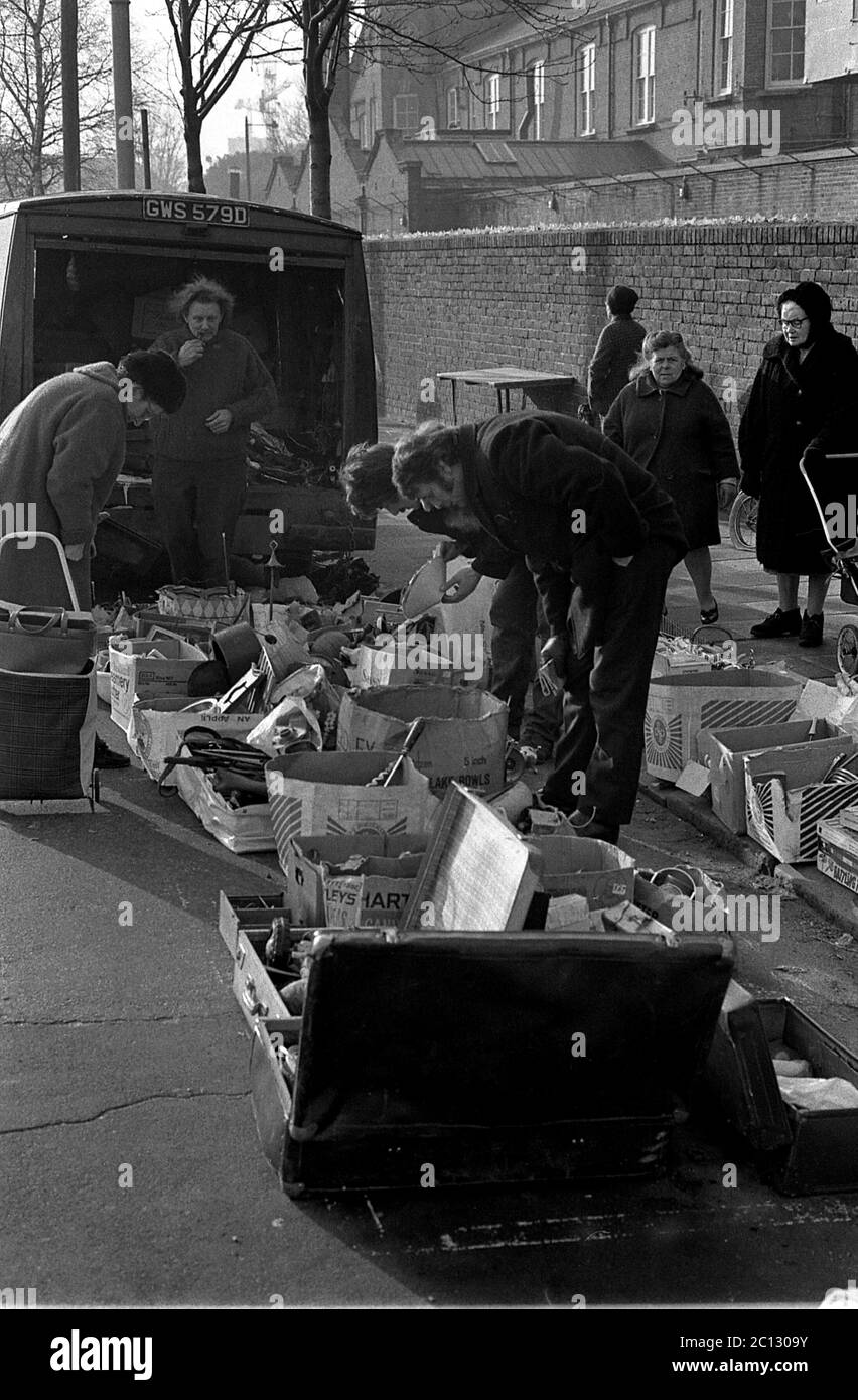 AJAXNETPHOTO. FEBRUAR 1975. PORTSMOUTH, ENGLAND. - FLOHMARKT - IN DER UNICORN ROAD; KÄUFER STÖBERN DURCH GEBRAUCHTE WAREN UND KLEIDUNG AUF DEM BÜRGERSTEIG.FOTO:JONATHAN EASTLAND/AJAX REF:7513 10 126 Stockfoto