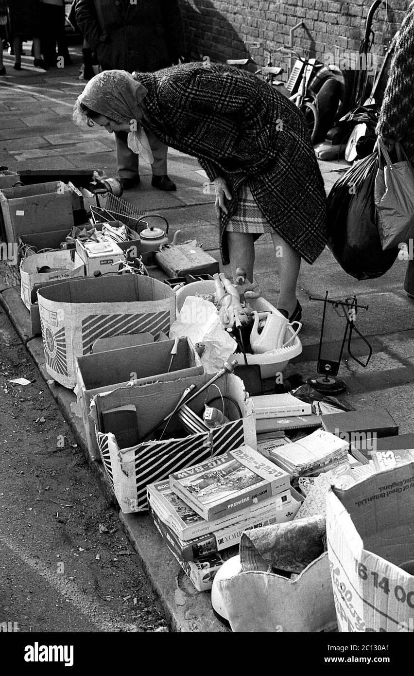 AJAXNETPHOTO. FEBRUAR 1975. PORTSMOUTH, ENGLAND. - FLOHMARKT - IN DER UNICORN ROAD; KÄUFER STÖBERN DURCH GEBRAUCHTE WAREN UND KLEIDUNG AUF DEM BÜRGERSTEIG.FOTO:JONATHAN EASTLAND/AJAX REF:7513 16 132 Stockfoto