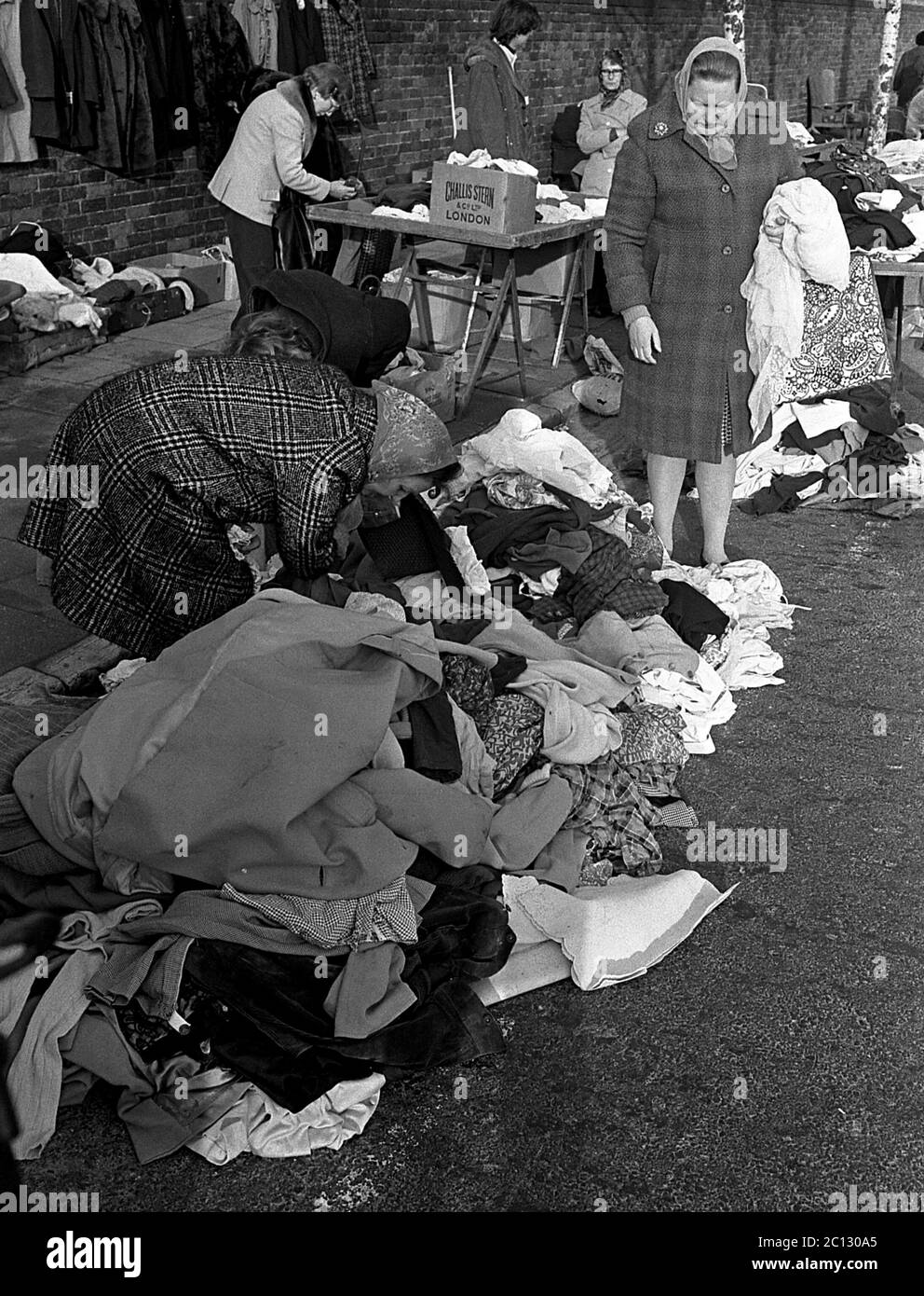 AJAXNETPHOTO. FEBRUAR 1975. PORTSMOUTH, ENGLAND. - FLOHMARKT - IN DER UNICORN ROAD; KÄUFER STÖBERN DURCH GEBRAUCHTE WAREN UND KLEIDUNG AUF DEM BÜRGERSTEIG.FOTO:JONATHAN EASTLAND/AJAX REF:7513 18 118 Stockfoto