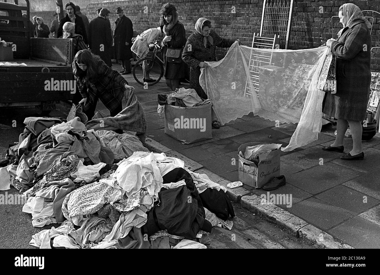 AJAXNETPHOTO. FEBRUAR 1975. PORTSMOUTH, ENGLAND. - FLOHMARKT - IN DER UNICORN ROAD; KÄUFER DURCHSTÖBERN GEBRAUCHTE WAREN UND KLEIDUNG AUF DEM BÜRGERSTEIG VERSTREUT; INSPEKTION EINES NET VORHANG.FOTO:JONATHAN EASTLAND/AJAX REF:7513 19A 119 Stockfoto