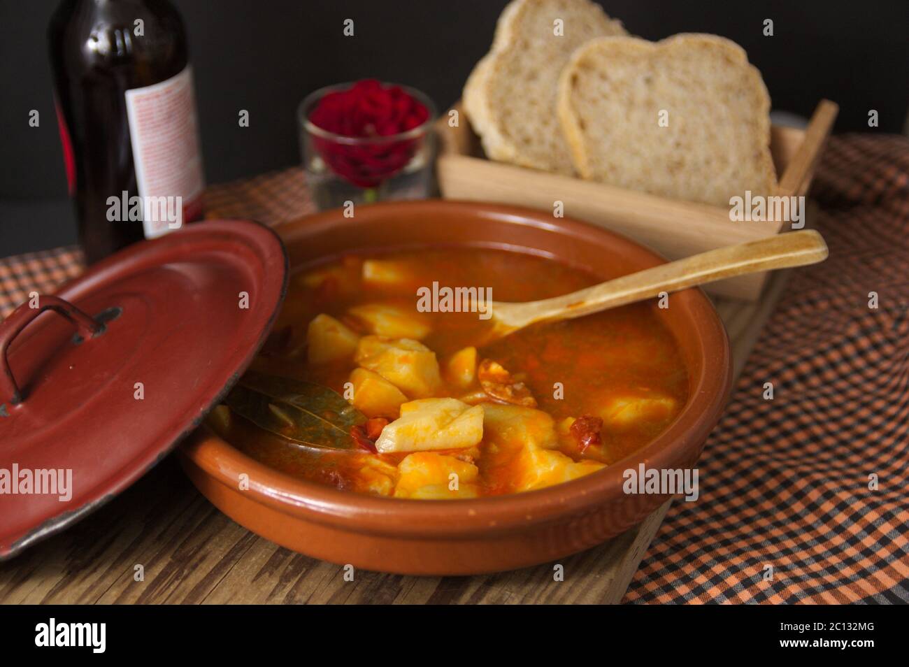 Präsentation der Kartoffelplatte im Rioja-Stil. Traditionelle spanische Speisen in einem Tontopf und einem Holzlöffel neben dem Brot und einem Flow serviert Stockfoto