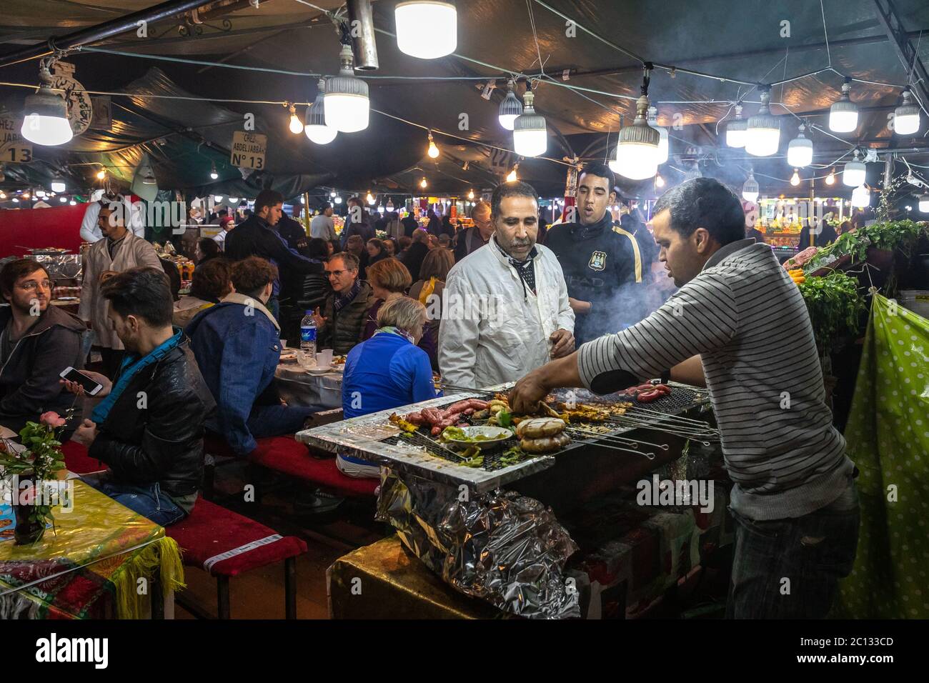 Straßenverkäufer, die auf dem Hauptplatz des Place Jemaa El Fna in Marrakesch, Marokko, nachts kochen und essen Stockfoto