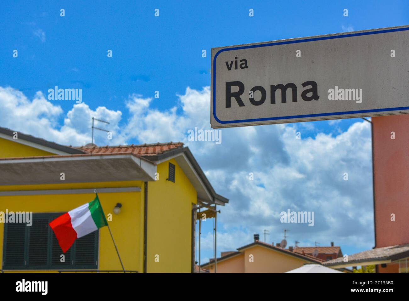 Patriotische Szene aus Italien: Rom Straße (Via Roma), die italienische Flagge (tricolore) und ein tiefblauer italienischer Himmel mit typischen mediterranen Häusern Stockfoto