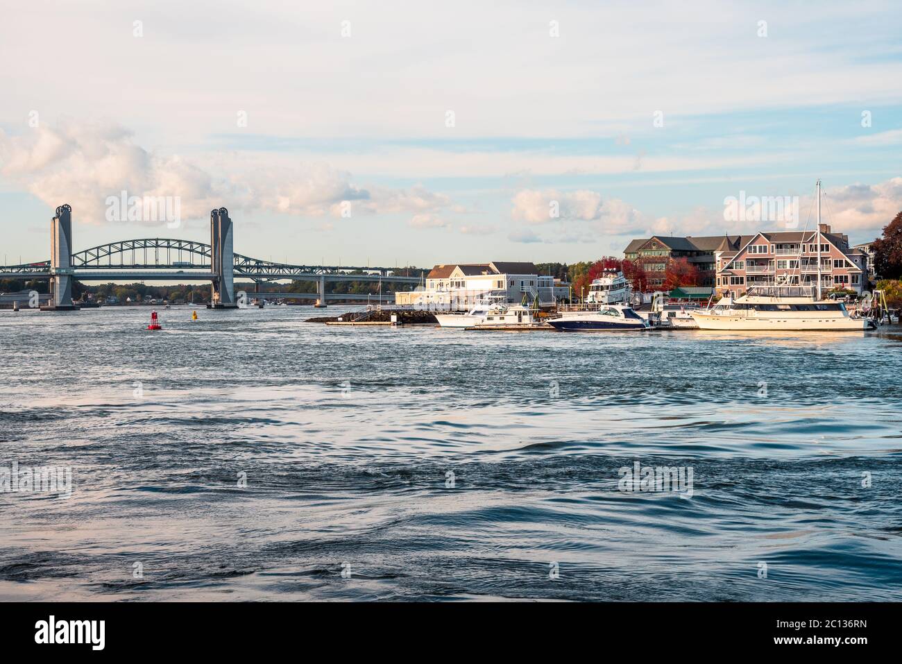 Luxusyachten, die an den Docks am Fluss festgemacht sind, mit einer Straßenbrücke, die im Hintergrund bei Sonnenuntergang zu sehen ist Stockfoto