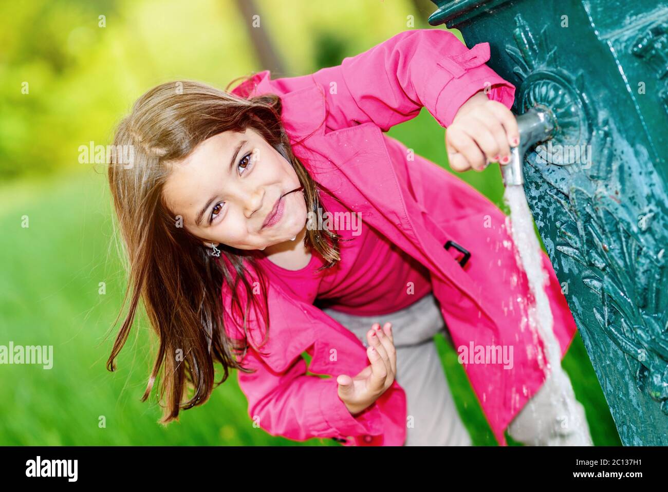 Nettes Kind, das gerade Wasser in einem Brunnen trinken will Stockfoto