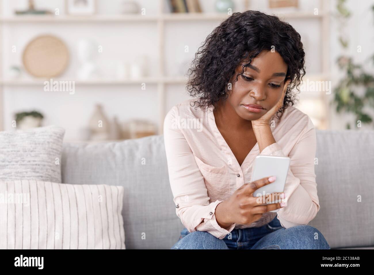 Warten auf seinen Anruf. Depressive schwarze Frau sitzt mit Handy zu Hause Stockfoto