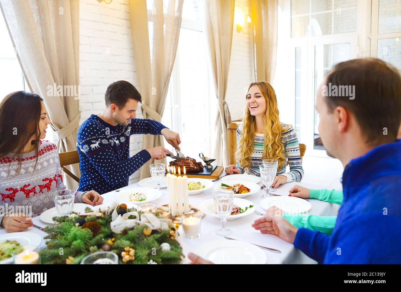 Freunde sitzen um einen Tisch und genießen Weihnachtsessen zusammen Stockfoto