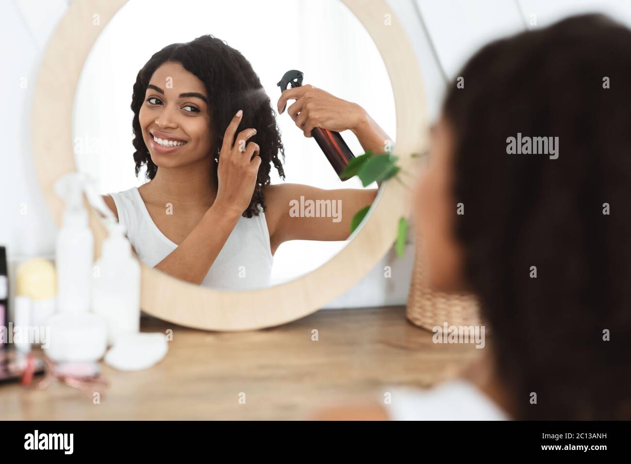 Frisur. Schöne Schwarze Frau Mit Haarspray Für Einfache Kämmen In Der Nähe Von Spiegel Stockfoto
