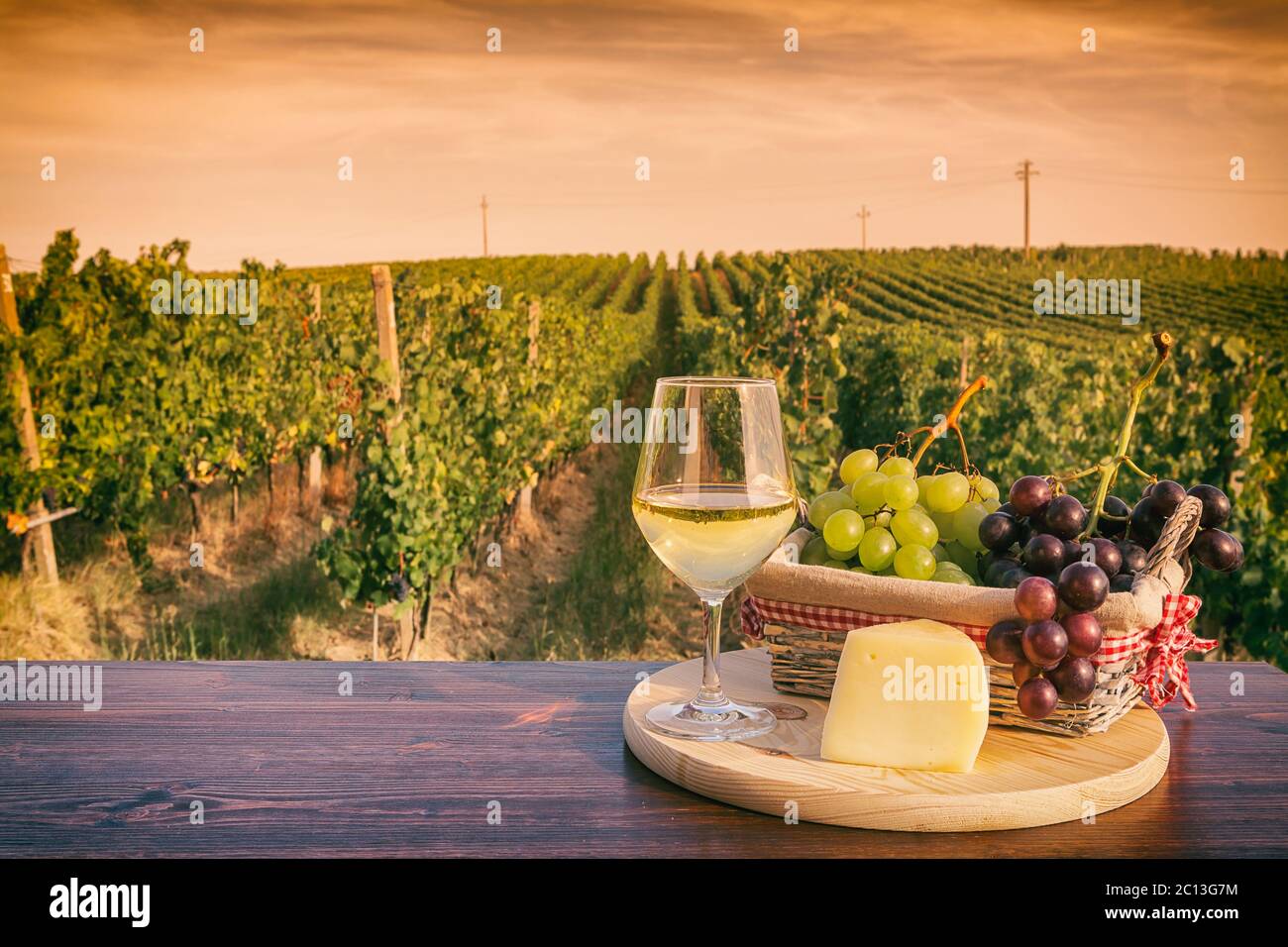 Glas Weißwein vor einem Weinberg bei Sonnenuntergang Stockfoto