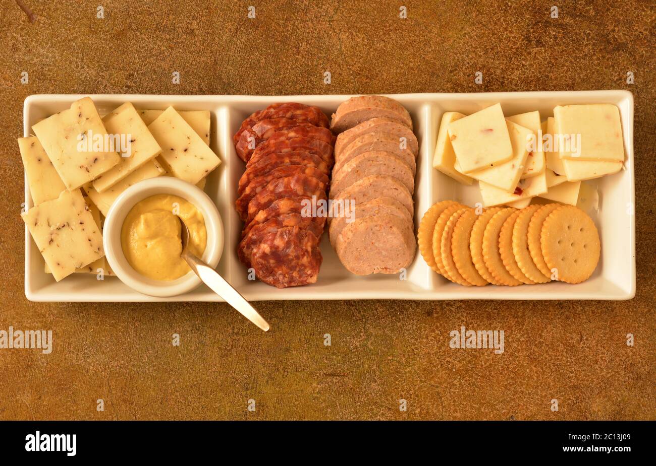 Ein rechteckiger Servierteller mit drei Fächern mit Käse, würziger Salami, Balogna, mit einem dijon-Senf. Stockfoto