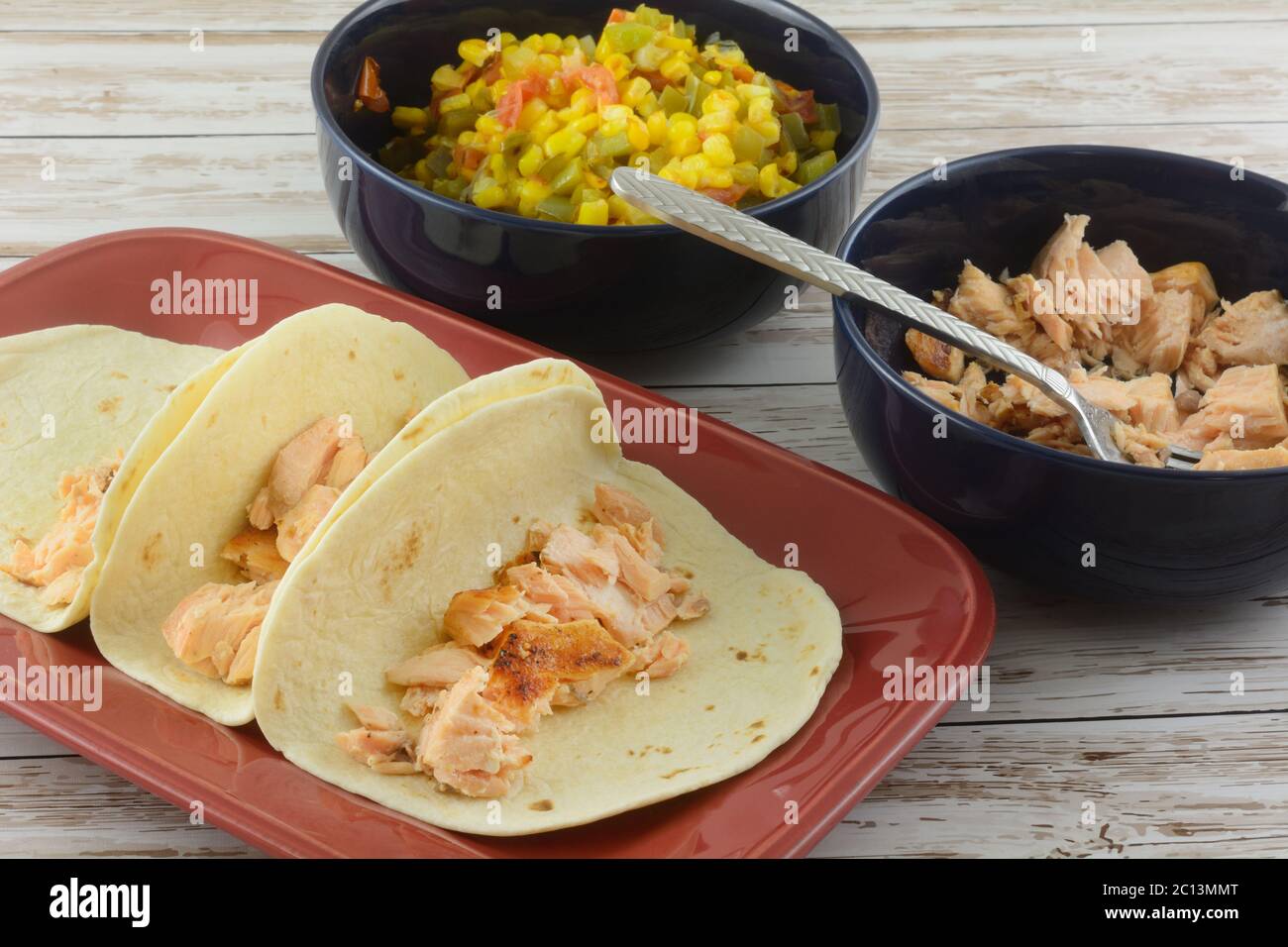 Lachs Tacos durch Setzen von Lachs in Tortillas auf Teller mit zwei Füllschalen gebackener Lachsfiletstücke und Mischung aus Mais, Tomaten, grün Stockfoto