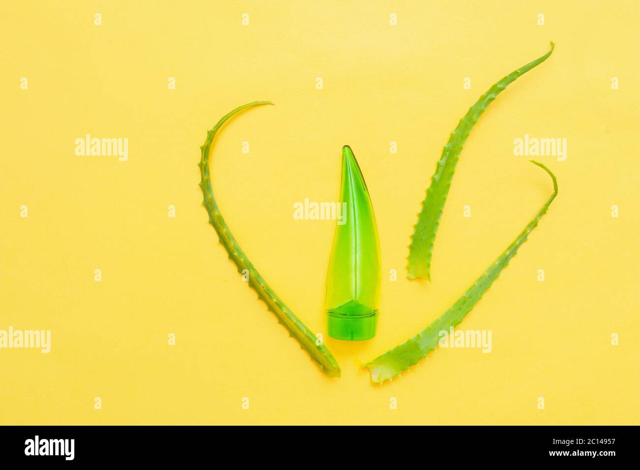 Grüne transparente Kosmetikröhre in Form eines Blattes aus Aloe und echte natürliche Blätter Aloe Vera auf einem gelben sauberen Hintergrund. Kosmetische Layout und Stockfoto