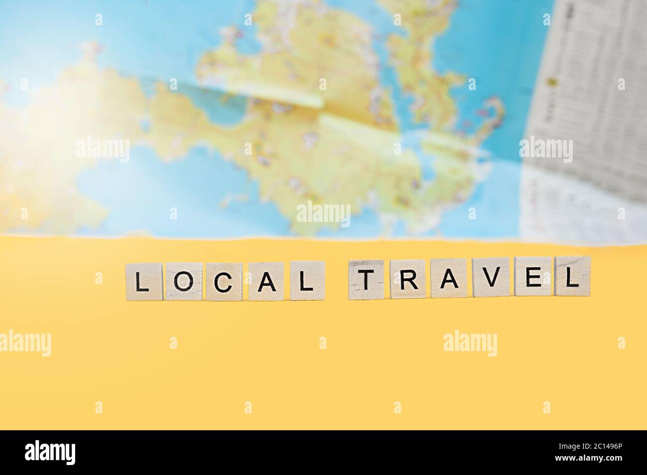 Lokale Reise-Schriftzug in quadratischen Holzbuchstaben auf hellem gelben Hintergrund und einer Karte. Relevante inländischen Tourismus 2020 Konzept Flatlay Stockfoto