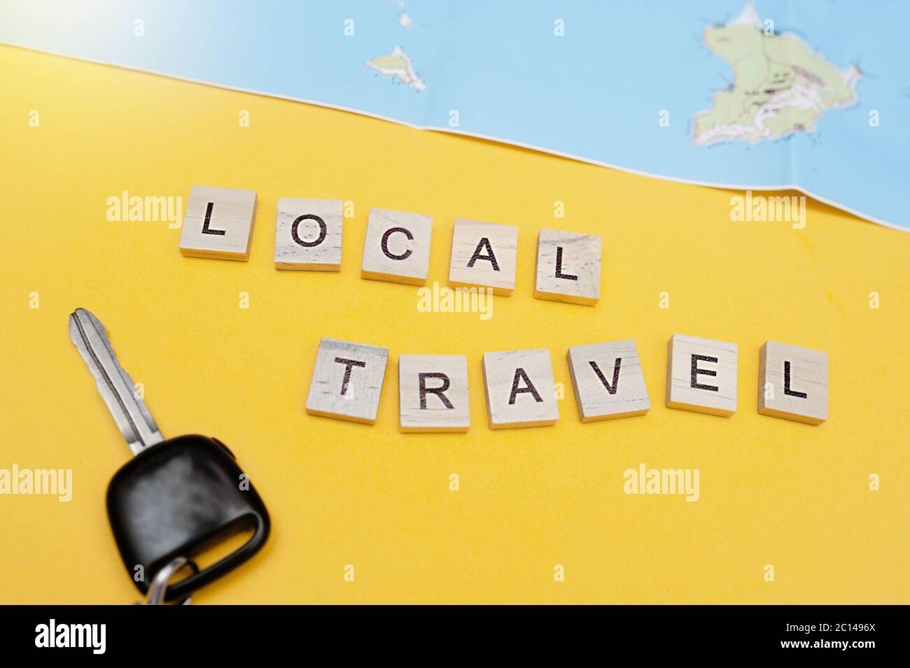 Lokale Reiseschriftzug in quadratischen Holzbuchstaben auf hellgelbem Hintergrund, Autoschlüssel und Touristenkarte. Lokaler Tourismus mit dem Auto und inländische Roadtrips Stockfoto