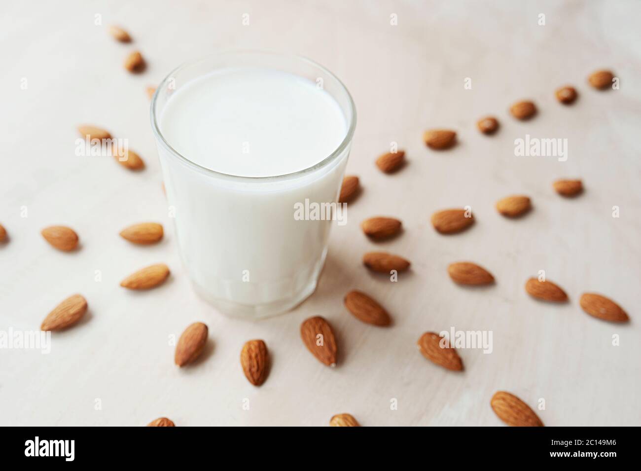 Durchsichtiger Becher voller Milch auf dem Hintergrund schön ausgebreitete Mandeln. Mandelmilch, Draufsicht Stockfoto