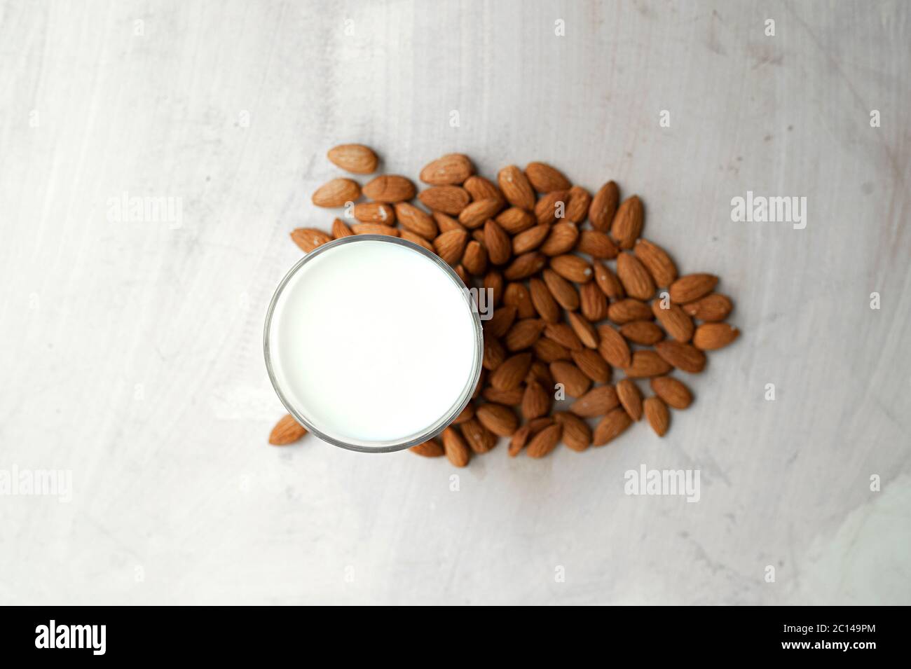 Durchsichtiger Becher voller Milch auf dem Hintergrund schön ausgebreitete Mandeln. Mandelmilch, Draufsicht Stockfoto