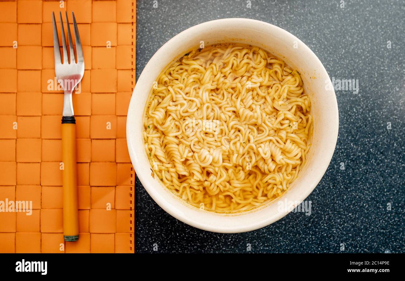 Instant Nudeln in Keramik-Schüssel auf orangefarbenem Hintergrund. Ist ein billiges, praktisches und einfaches Menü. Sparen Sie Geld während der weltweiten Finanzkrise Stockfoto
