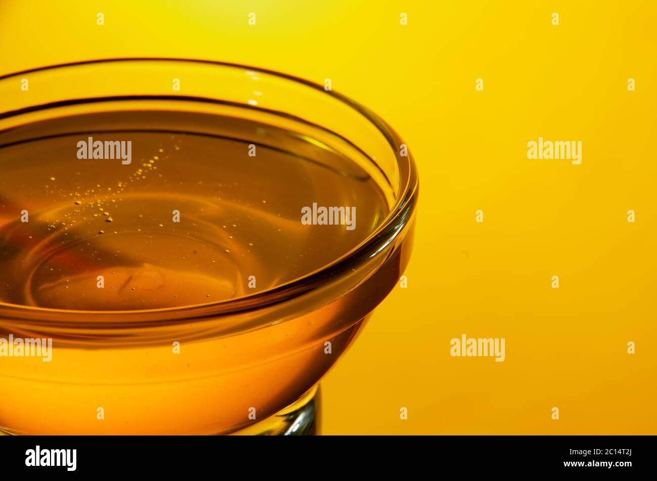 Nahaufnahme einer kleinen Glasschale mit Honig auf gelbem Hintergrund mit Hintergrundbeleuchtung. Geringer Fokus. Stockfoto